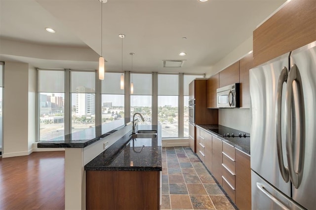 kitchen with appliances with stainless steel finishes, dark stone counters, sink, hanging light fixtures, and an island with sink