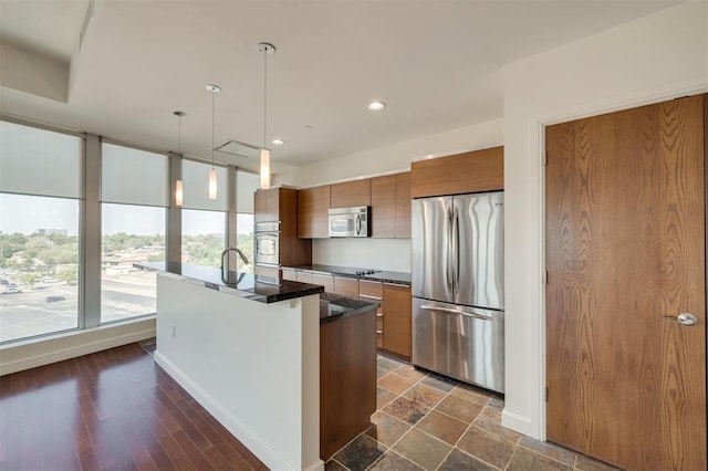 kitchen featuring an island with sink, stainless steel appliances, hanging light fixtures, and sink