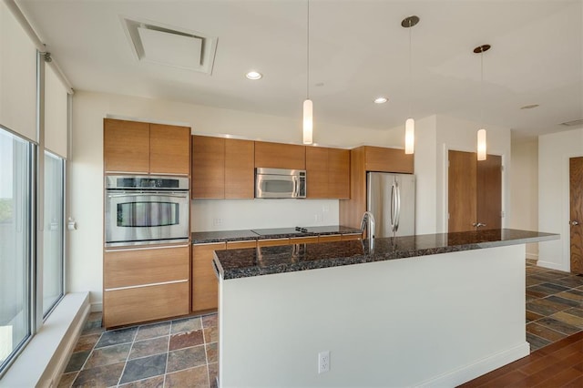 kitchen with a kitchen island with sink, dark stone counters, decorative light fixtures, and appliances with stainless steel finishes