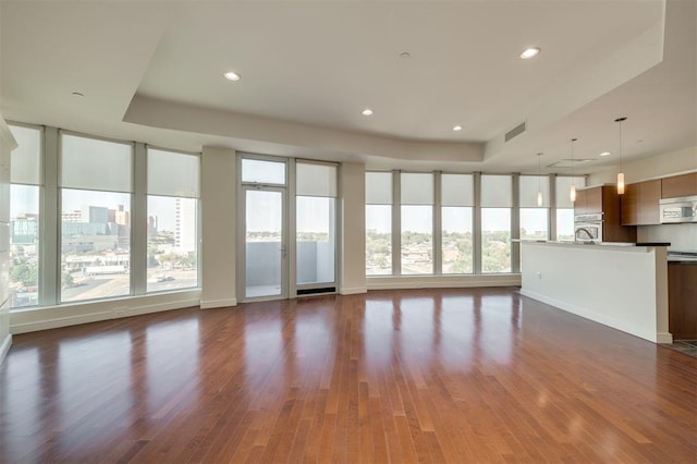 unfurnished living room featuring a healthy amount of sunlight, dark wood-type flooring, and a tray ceiling