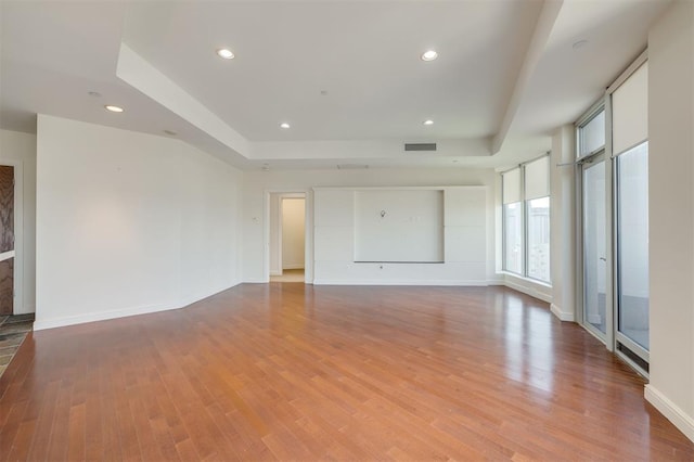 unfurnished living room with light wood-type flooring and a raised ceiling