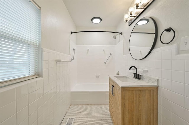 bathroom with tile patterned flooring, vanity, tile walls, and tiled shower / bath