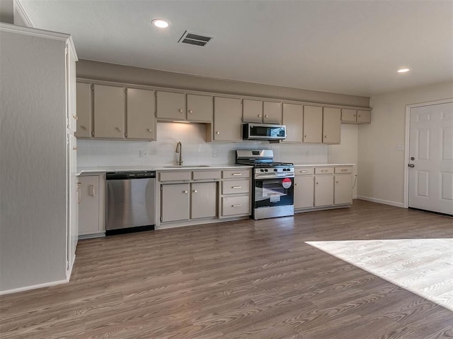 kitchen with backsplash, sink, stainless steel appliances, and light hardwood / wood-style floors