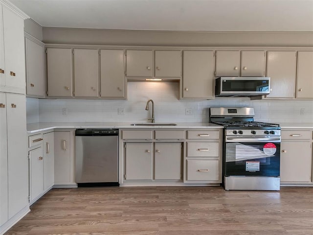 kitchen with tasteful backsplash, sink, light hardwood / wood-style floors, and appliances with stainless steel finishes