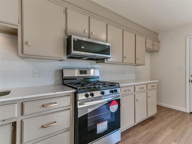 kitchen featuring decorative backsplash, appliances with stainless steel finishes, and light hardwood / wood-style floors