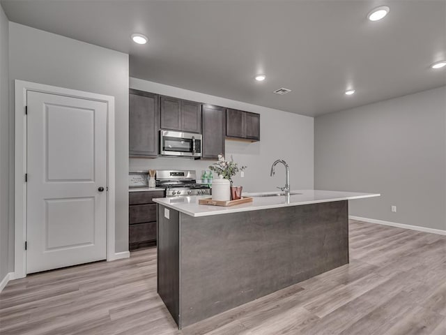 kitchen with sink, dark brown cabinetry, a kitchen island with sink, and appliances with stainless steel finishes