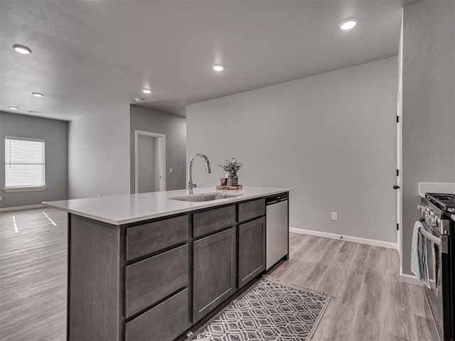 kitchen featuring sink, an island with sink, appliances with stainless steel finishes, dark brown cabinets, and light hardwood / wood-style floors