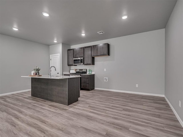 kitchen featuring sink, stainless steel appliances, an island with sink, dark brown cabinets, and light wood-type flooring