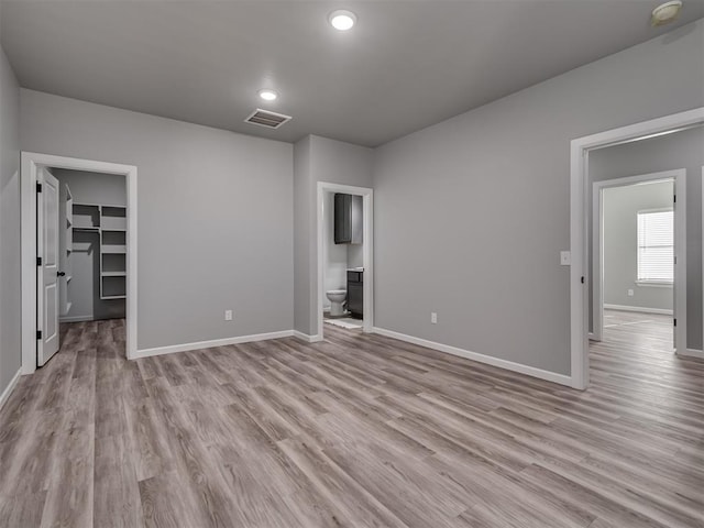 unfurnished bedroom featuring ensuite bathroom, light hardwood / wood-style floors, a walk in closet, and a closet