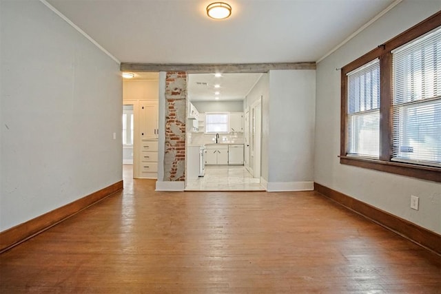 unfurnished living room featuring light hardwood / wood-style floors, decorative columns, crown molding, and sink