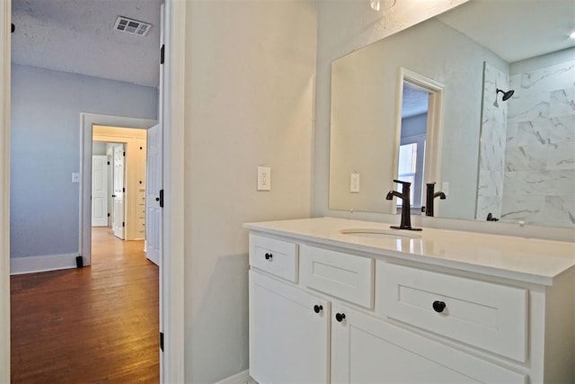 bathroom with hardwood / wood-style flooring, vanity, and a tile shower