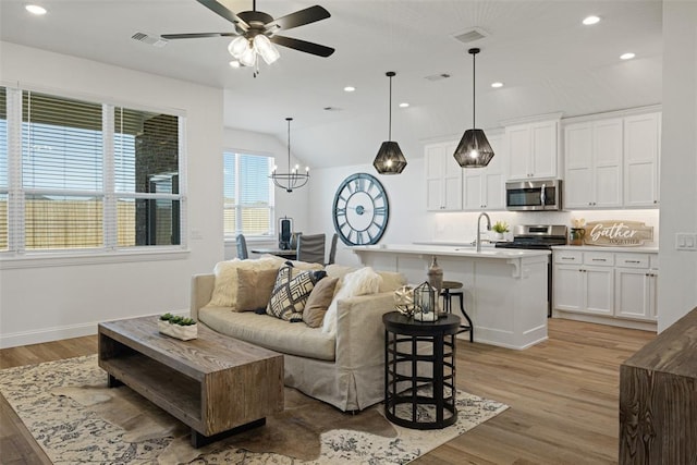 living room featuring ceiling fan with notable chandelier, light hardwood / wood-style floors, sink, and vaulted ceiling