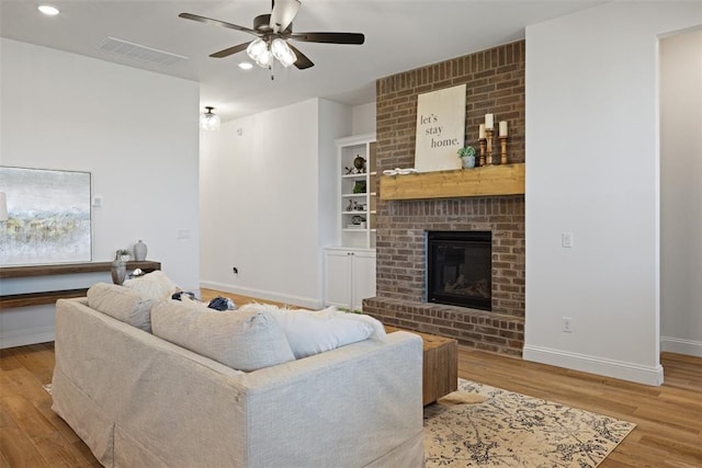 living room featuring ceiling fan, light hardwood / wood-style flooring, and a brick fireplace