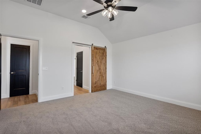 unfurnished bedroom with a barn door, ceiling fan, light colored carpet, and lofted ceiling