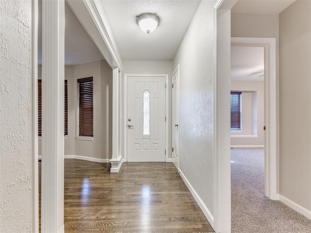 foyer entrance featuring a textured ceiling and dark colored carpet