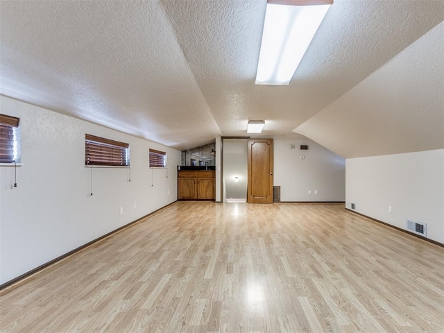 additional living space featuring lofted ceiling, a textured ceiling, and light hardwood / wood-style floors