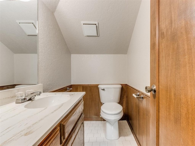 bathroom featuring vaulted ceiling, vanity, wooden walls, and toilet