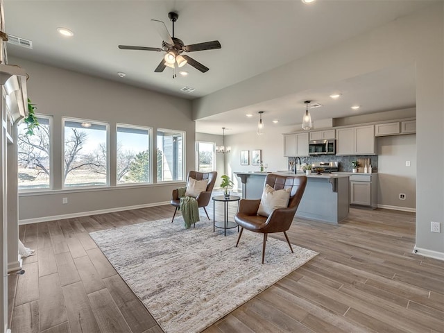 living room featuring ceiling fan with notable chandelier, light hardwood / wood-style flooring, and sink