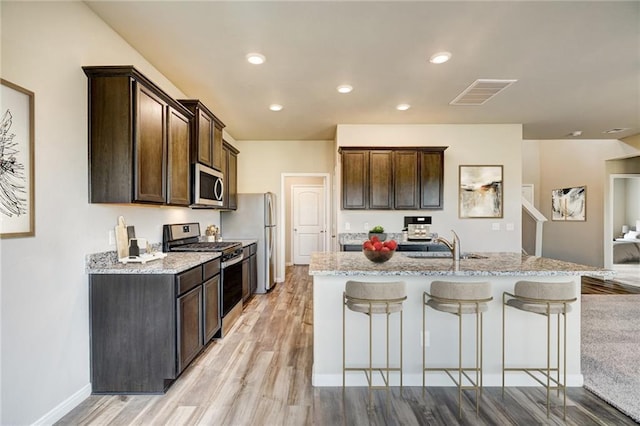 kitchen with light stone countertops, sink, light hardwood / wood-style flooring, an island with sink, and appliances with stainless steel finishes