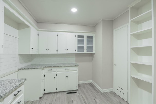 kitchen featuring light stone counters, white cabinetry, light hardwood / wood-style flooring, and decorative backsplash