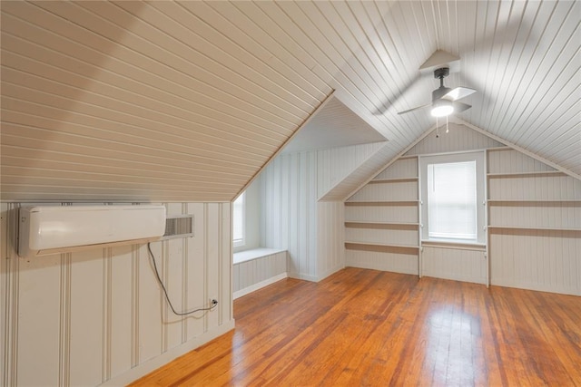 additional living space featuring wooden walls, hardwood / wood-style floors, vaulted ceiling, and a wall unit AC