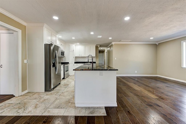 kitchen with appliances with stainless steel finishes, an island with sink, dark stone counters, white cabinets, and ornamental molding