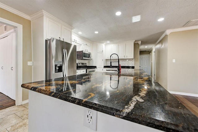 kitchen featuring white cabinetry, sink, stainless steel appliances, backsplash, and dark stone countertops