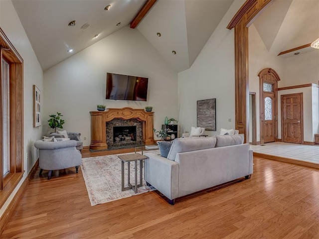 living room featuring a high end fireplace, light hardwood / wood-style flooring, high vaulted ceiling, and beamed ceiling