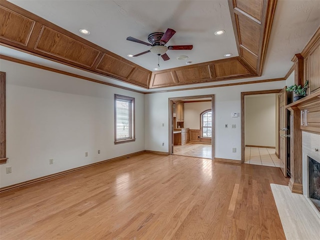 unfurnished living room featuring ornamental molding, ceiling fan, a tray ceiling, a high end fireplace, and light hardwood / wood-style floors