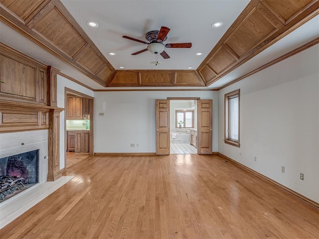 unfurnished living room featuring a premium fireplace, crown molding, ceiling fan, and light hardwood / wood-style flooring