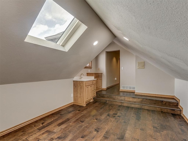 bonus room featuring dark wood-type flooring, lofted ceiling with skylight, sink, and a textured ceiling