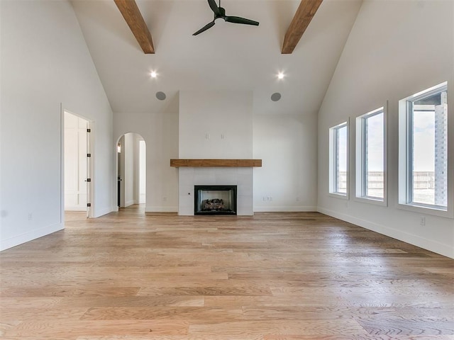 unfurnished living room featuring ceiling fan, baseboards, beam ceiling, and light wood-style floors