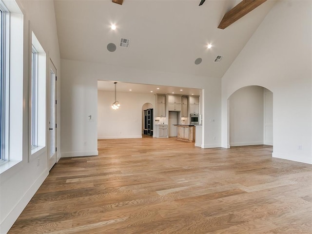 unfurnished living room with high vaulted ceiling, arched walkways, visible vents, and light wood-style flooring