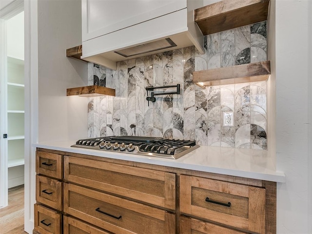 kitchen with custom range hood, light countertops, backsplash, brown cabinets, and stainless steel gas stovetop