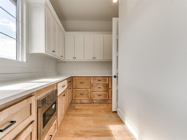 kitchen featuring light countertops, stainless steel microwave, light wood-type flooring, and white cabinets