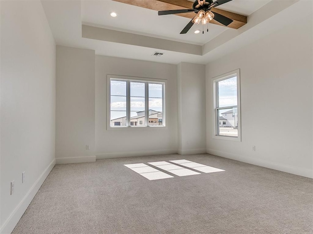 empty room featuring a raised ceiling, carpet flooring, visible vents, and baseboards