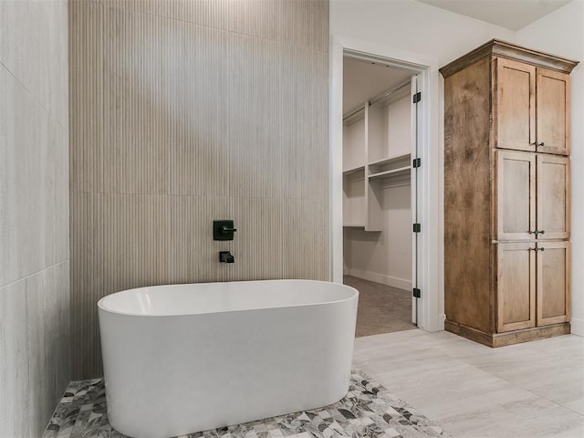 bathroom featuring a freestanding tub, a walk in closet, and tile walls