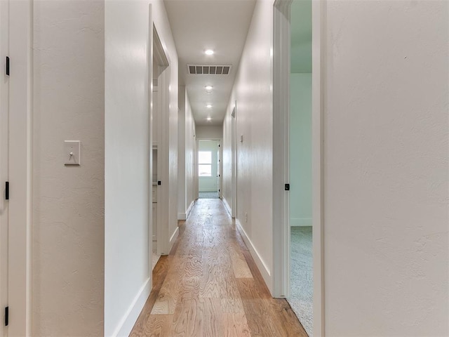 hallway with visible vents, light wood-style flooring, and baseboards