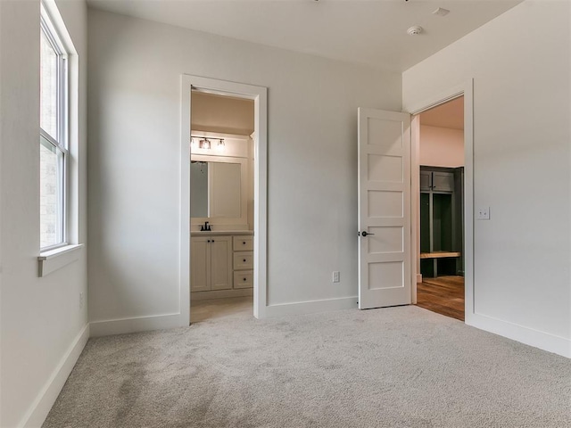 unfurnished bedroom with light colored carpet, ensuite bath, baseboards, and multiple windows