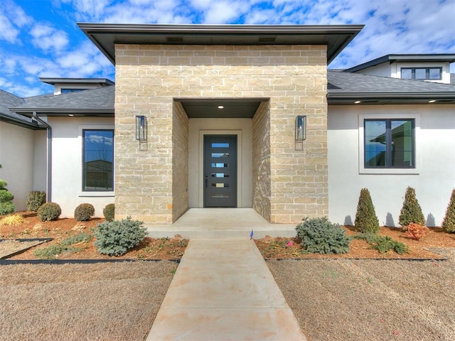 entrance to property featuring stone siding, stucco siding, and roof with shingles