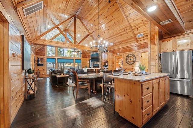 kitchen featuring wooden walls, decorative light fixtures, high vaulted ceiling, a kitchen island, and stainless steel refrigerator