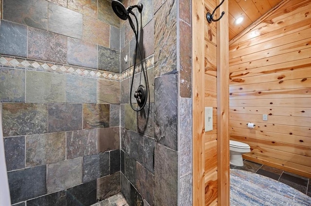 bathroom featuring tiled shower, wooden walls, toilet, and lofted ceiling