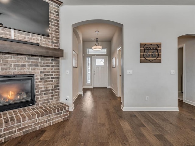 foyer entrance with a brick fireplace and dark wood-type flooring