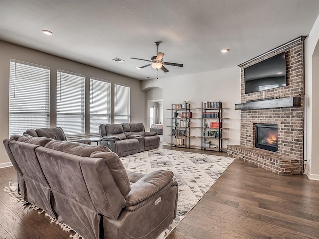 living room featuring dark hardwood / wood-style flooring, a brick fireplace, and ceiling fan