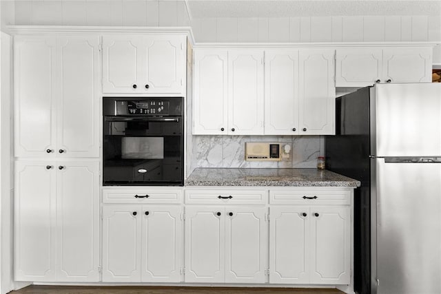 kitchen with decorative backsplash, stainless steel fridge, white cabinetry, and black oven