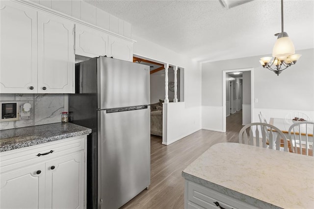 kitchen featuring stainless steel fridge, a textured ceiling, white cabinetry, and hanging light fixtures