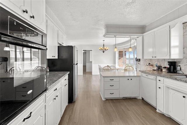 kitchen featuring hanging light fixtures, white dishwasher, light hardwood / wood-style floors, black oven, and white cabinets