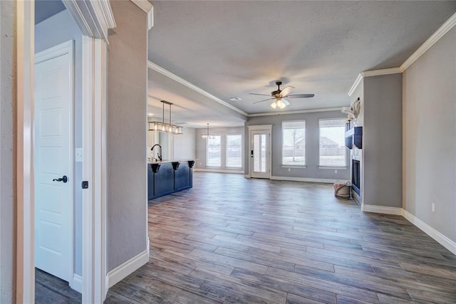 unfurnished living room with ceiling fan with notable chandelier, dark hardwood / wood-style floors, and crown molding