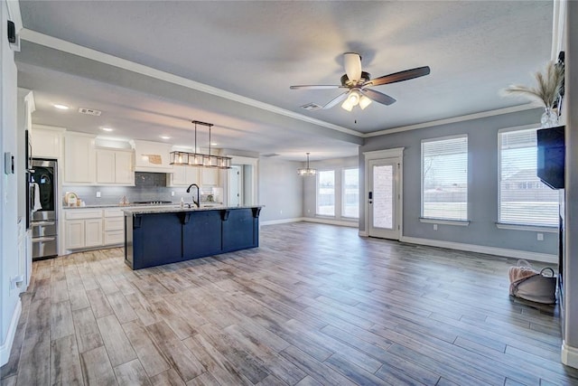 kitchen featuring light wood-type flooring, ceiling fan, white cabinetry, hanging light fixtures, and an island with sink