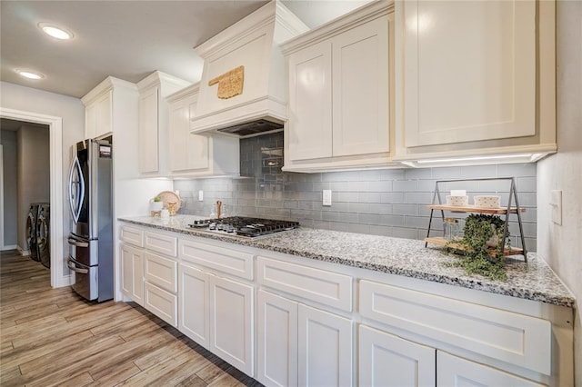 kitchen with decorative backsplash, light stone counters, light wood-type flooring, and stainless steel appliances